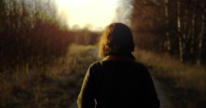 Girl walking into frame on path in the forest during sunset
