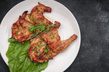 Fried tobacco chicken with a leaf of lettuce on a plate, on a dark background