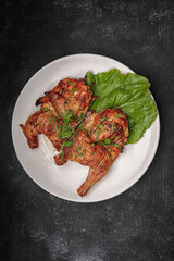 Fried tobacco chicken with a leaf of lettuce on a plate, on a dark background
