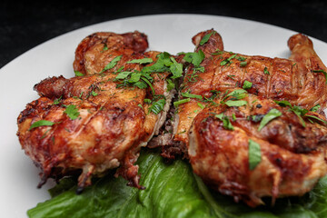 Fried tobacco chicken with a leaf of lettuce on a plate, on a dark background