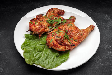 Fried tobacco chicken with a leaf of lettuce on a plate, on a dark background