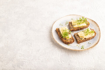 Grain bread sandwiches with cheese and watercress microgreen on gray concrete, side view, copy space.