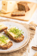 Grain bread sandwiches with cheese and watercress microgreen on gray concrete, side view, selective focus.