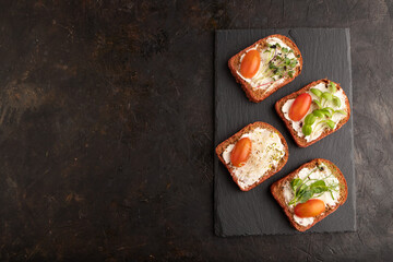 Red beet bread sandwiches with cream cheese, tomatoes and microgreen on black. top view.