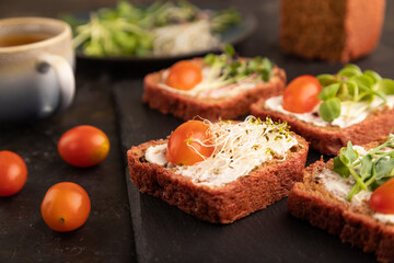 Red beet bread sandwiches with cream cheese, tomatoes and microgreen on black. side view, selective focus.