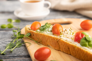 Long white bread sandwich with cream cheese, tomatoes and microgreen on gray. side view, selective focus.