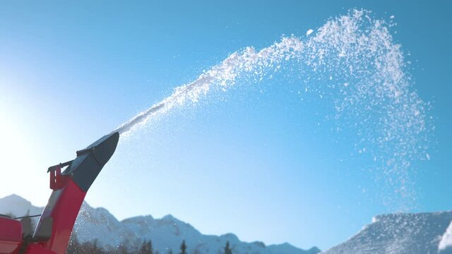 SLOW MOTION, CLOSE UP, COPY SPACE: Industrial snow blower spews out snowflakes into the sunny sky as unknown shaper makes kickers in the snowpark of Vogel ski resort. Machine is blowing out snow.