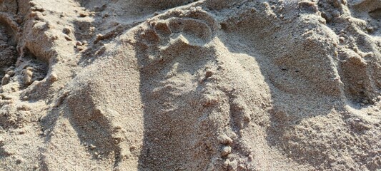 Beach sand in the rays of the summer sun. Sunny day on the shore. The yellow-brown sand is uneven with dents and footprints of people. Bumps in the sand cast dark shadows from the sun.