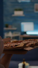 Caucasian woman putting pizza order on table in living room preparing to eat while watching movie on TV at home. Young person using delivery concept for takeaway food eating indoors