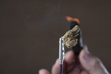 Smoking herb hold by tweezers on a brown background