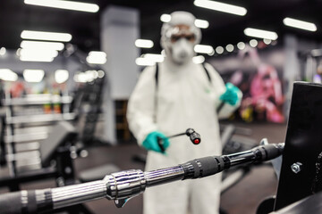 Fototapeta na wymiar Expert warning on the serious epidemiological situation of coronavirus. Cleaning and disinfection of exercise space and gym equipment. A man in protective clothing uses a sprayer with chemicals