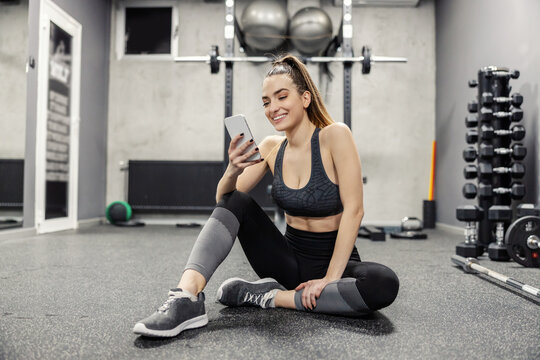 Sports lifestyle and dependence on social networks. A female dressed in sports clothes uses the phone during training. She posts photos and videos from the training on social networks