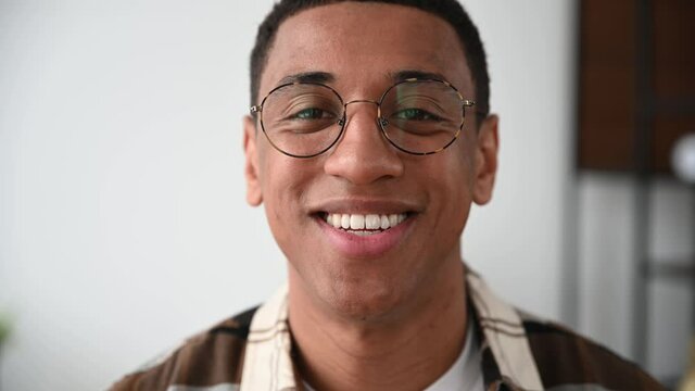 Close-up video portrait of a handsome positive millennial hispanic guy with glasses, freelancer or student, standing indoors, looking directly at the camera, smiling friendly