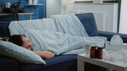 Sick woman laying on couch with blanket feeling cold and having virus symptoms. Adult with seasonal...