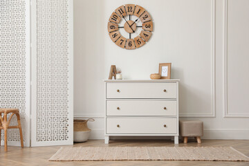 Stylish room with wooden folding screen and chest of drawers near white wall. Interior design