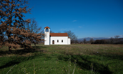 Fototapeta premium A view of a village church. The beautiful church yard with a huge meadow and a beautiful sky above. A lonely church waiting for people to stop by.