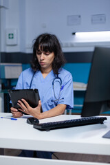 Woman nurse looking at digital tablet for practice at night. Medical assistant using modern device with technology and touch screen for healthcare, working late. Physician with job