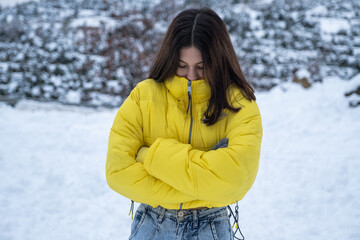 young woman in yellow coat chilling outside in snowy weather,young woman smiling at camera in front of natural background in snowy weather