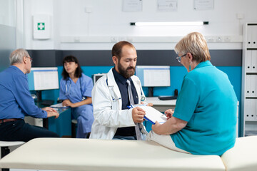 Retired woman signing checkup documents and talking to doctor for treatment. Medic asking patient...