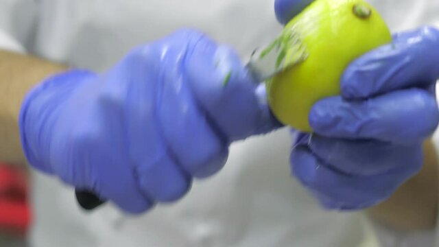 A close-up of a chef in blue gloves with a lemon in his hands peeling lemon peel. Preparation for cooking. Seafood. Fine cuisine in an elite restaurant