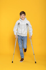 Teenage boy with injured leg using crutches on yellow background