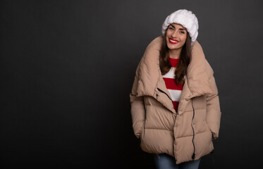 Close up portrait of a beautiful smiling woman in a winter hat and warm stylish puffer while she...