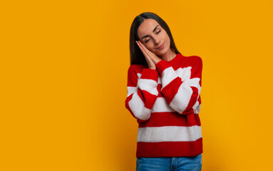 Time to sleep and relax. Portrait of a beautiful calmed young girl in a winter sweater isolated on the yellow background while she is preparing to sleep