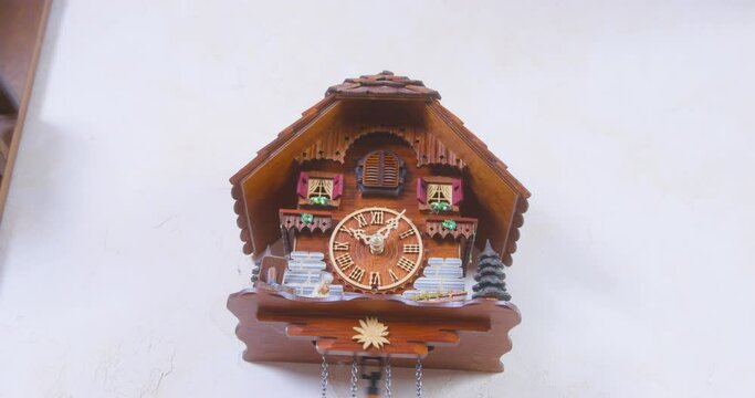 Creative wooden house-shaped wall clock with fast swinging pendulum hanging on empty white wall IN room at home close view