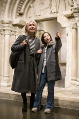 Full length portrait of positive intelligent senior woman and cute interested preteen girl viewing...