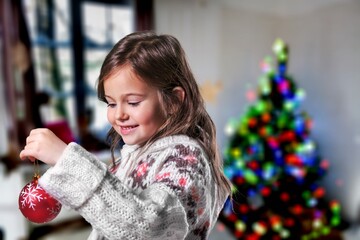 Cheerful small girl indoors at home at Christmas, holding decor.