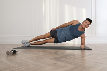 Handsome man doing side plank exercise on yoga mat indoors
