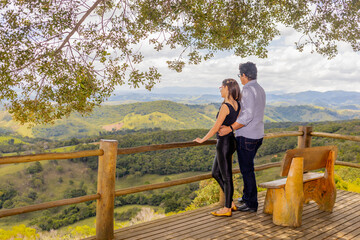 Fototapeta na wymiar Casal em uma montanha assistindo o entardecer com uma bela paisagem de montanhas e natureza ao fundo