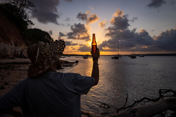 Young man in a rustic hat having a beer on the beach.