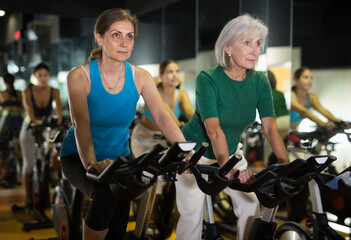 Fototapeta na wymiar Portrait of middle-aged and elderly women training together during stationary bike workout in fitness center
