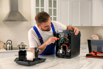 Repairman with screwdriver fixing coffee machine at table in kitchen