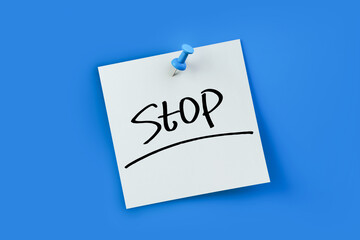 stop written on white sticker note over blue background