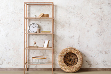 Wooden bookcase with decor and rattan pouf near light wall