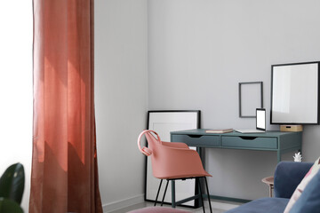 Modern workplace with laptop and blank frames hanging on light wall