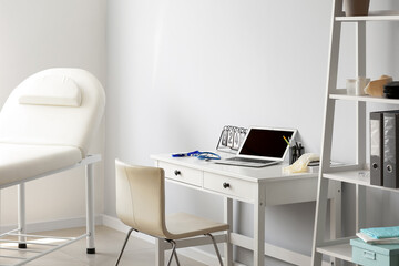 Doctor's workplace with laptop near light wall in medical office