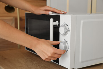 Woman switching on microwave oven in kitchen, closeup