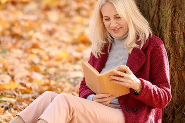 Mature woman reading book in autumn park