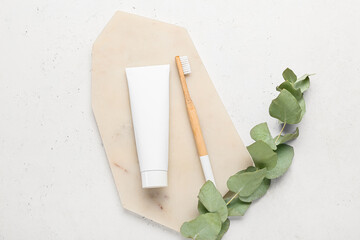 Wooden toothbrush, paste and eucalyptus branch on light background
