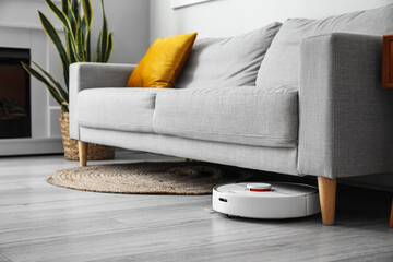 Modern robot vacuum cleaner near sofa in room - obrazy, fototapety, plakaty