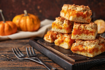 Wooden board with pieces of tasty pumpkin pie on table