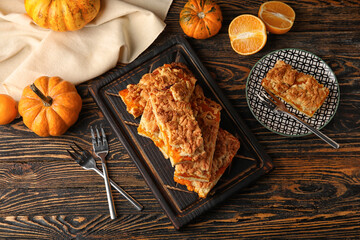 Plate and board with pieces of tasty pumpkin pie on wooden background