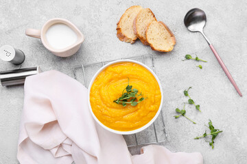 Bowl of tasty pumpkin cream soup and bread on grey background