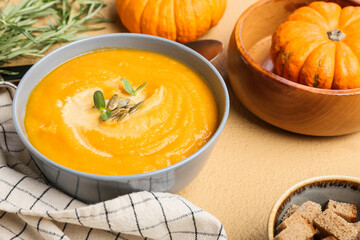 Bowl of tasty pumpkin cream soup on beige background