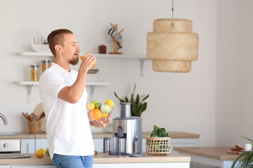 Young man with glass of fresh fruit juice near modern juicer in kitchen