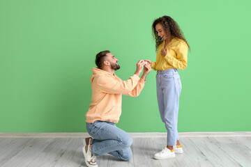 Young man proposing to his girlfriend on color background