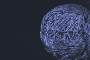A ball of yarn on a black background. Material for knitting. Home crafts and hobbies. Colored in trendy color of year 2022 Very Peri. Selective focus, copy space.